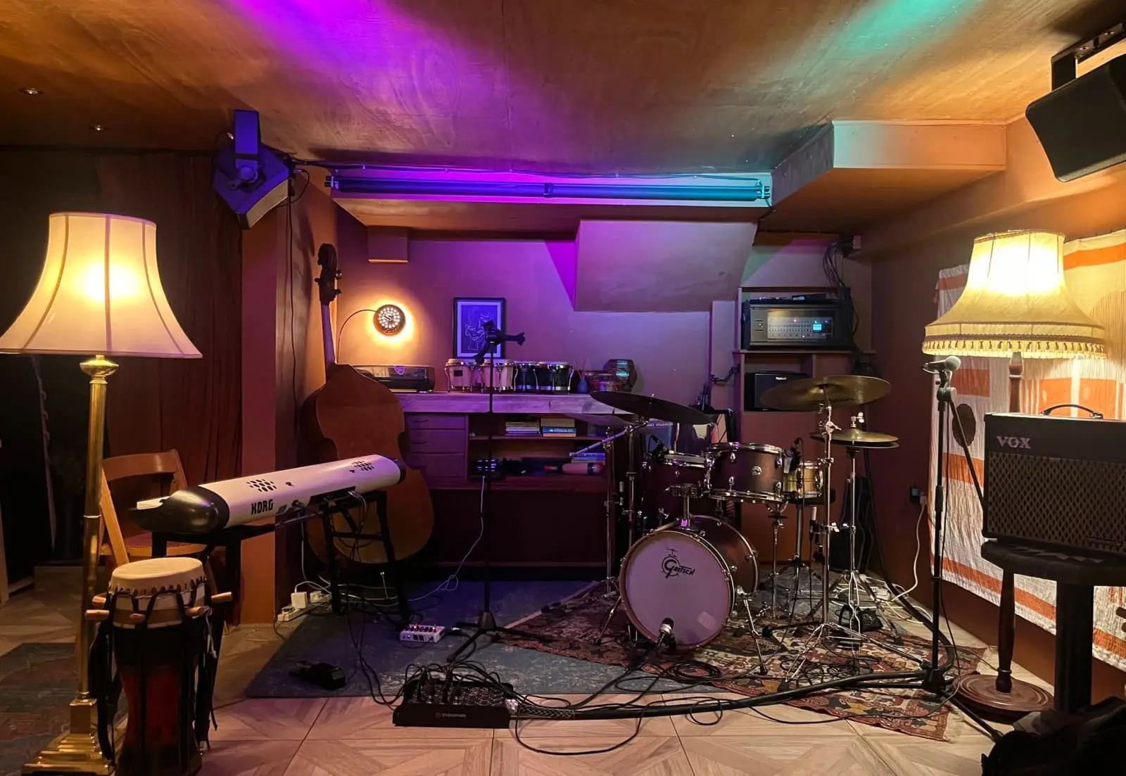 The basement live room: a drum kit on the stage between two standard lamps, under purple light
