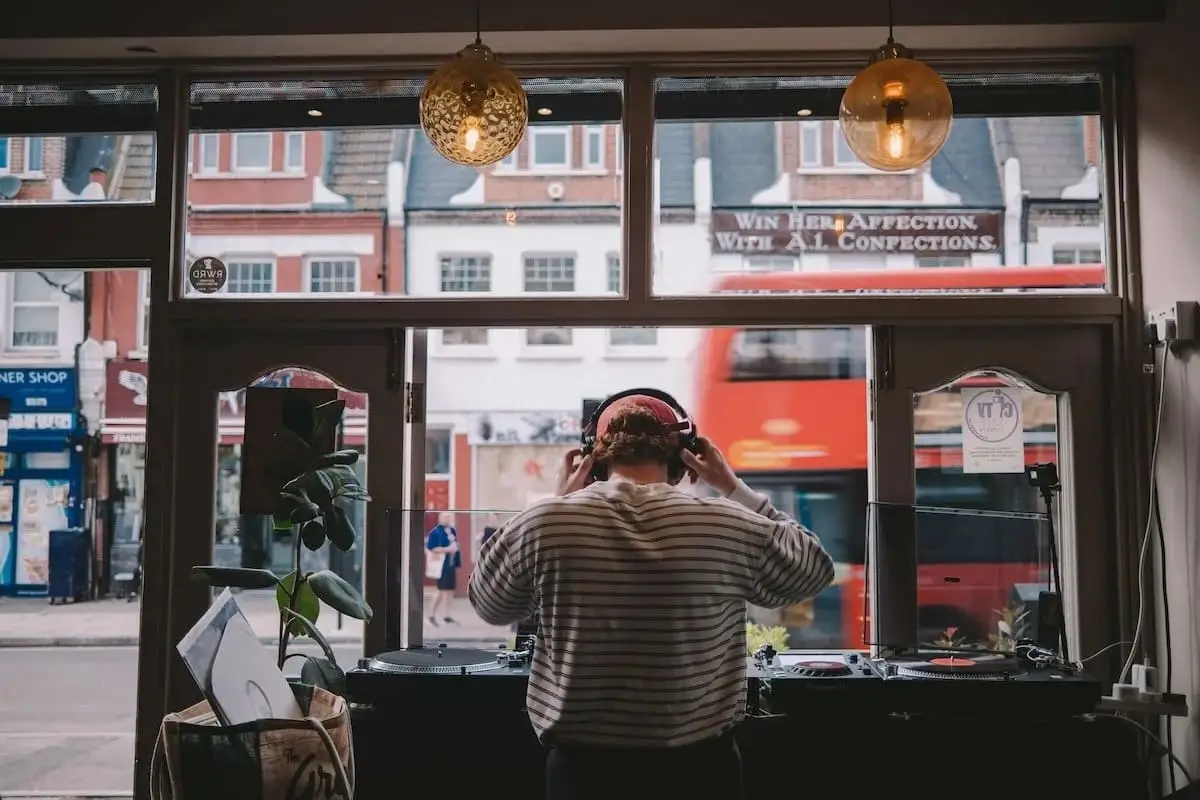 A DJ in headphones at the decks in the front window, with Albion Road and a red bus behind
